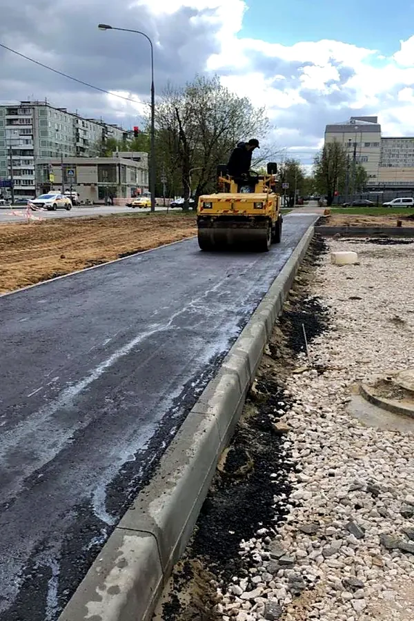 Уплотнение асфальта пешеходной дорожки катком вдоль установленного бортового камня