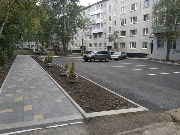 Готовый двор: асфальтованная парковка с разметкой, плитка, газон и высаженные кустарники у панельного дома