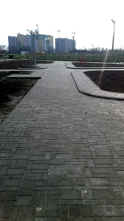 Дорожки из серой тротуарной плитки в новом сквере с фонарями и подготовленными клумбами